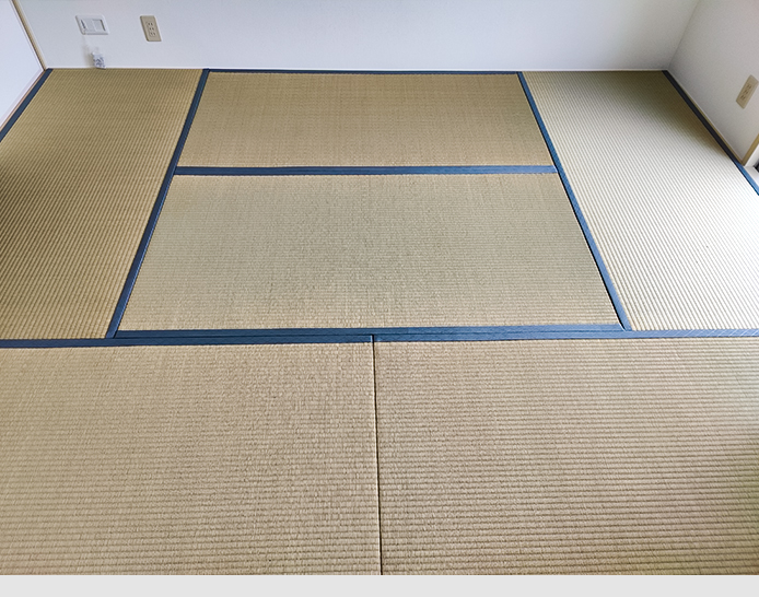 Schlafzimmerboden mit Tatami-Matten. Sechs große Bodenmatten aus Stroh bilden den Boden des Schlafzimmers. Am Rand sind die Matten mit einem dunkelgrauen Textilband eingefasst.