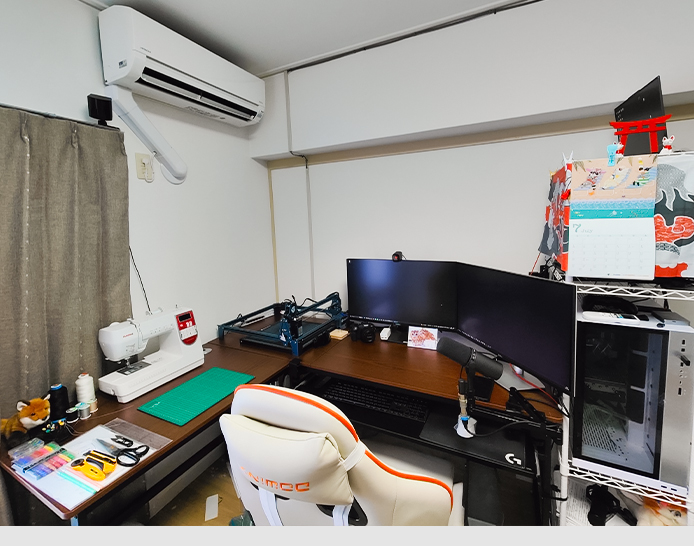 Yasuyukis Remote-Arbeitsplatz besteht aus einem dunkelbraunen Eckschreibtisch. Auf einem ausziehbaren Brett liegen Tastatur und Maus. An der Seite ist ein Mikrofon an der Tischplatte befestigt. Auf dem Tisch stehen zwei Bildschirme und eine Webcam.